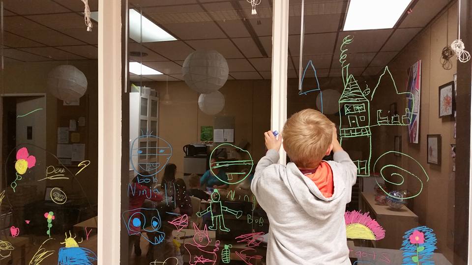 A young boy is drawing on a window with chalk.