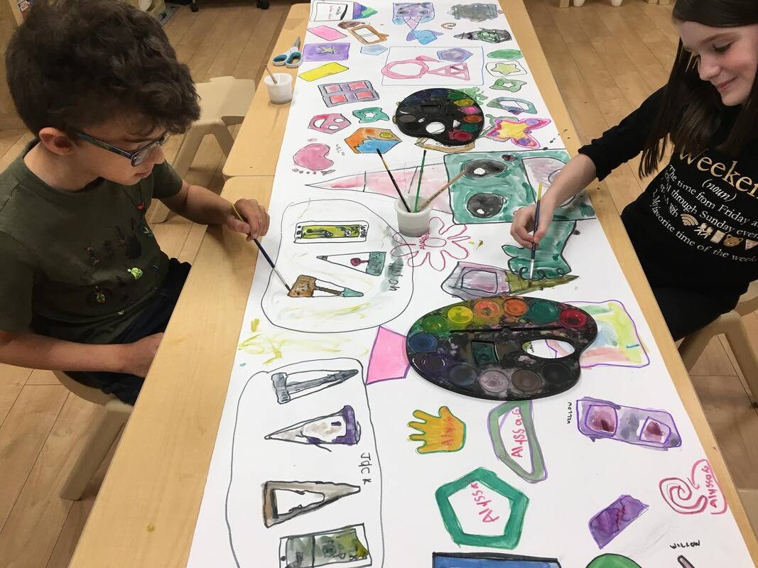A boy and a girl are sitting at a table painting on a large piece of paper.