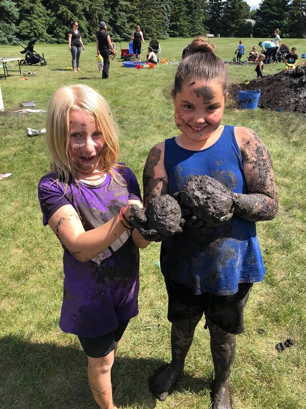 Two young girls are standing next to each other in a field covered in mud.