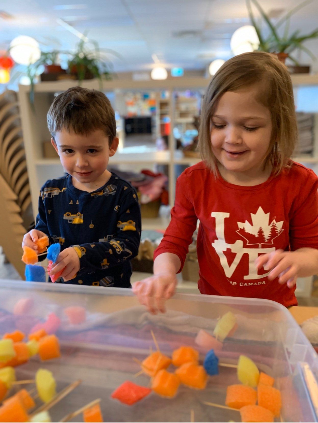 A boy and a girl are playing with watermelon cubes in a plastic container.