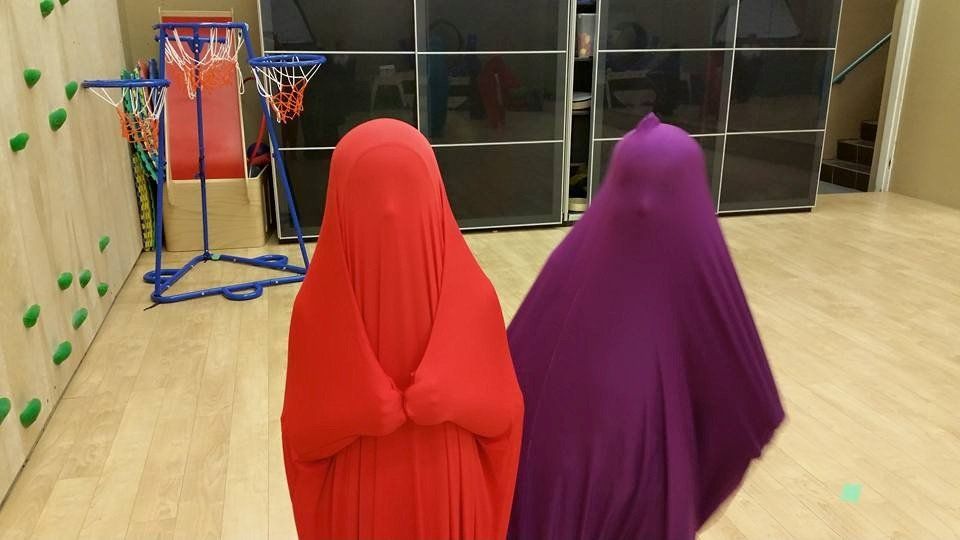 Three people are standing next to each other in a room with a basketball hoop in the background.