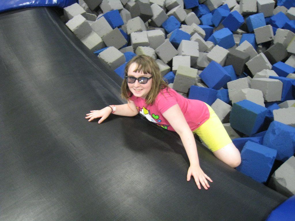 A little girl wearing sunglasses is crawling on a trampoline