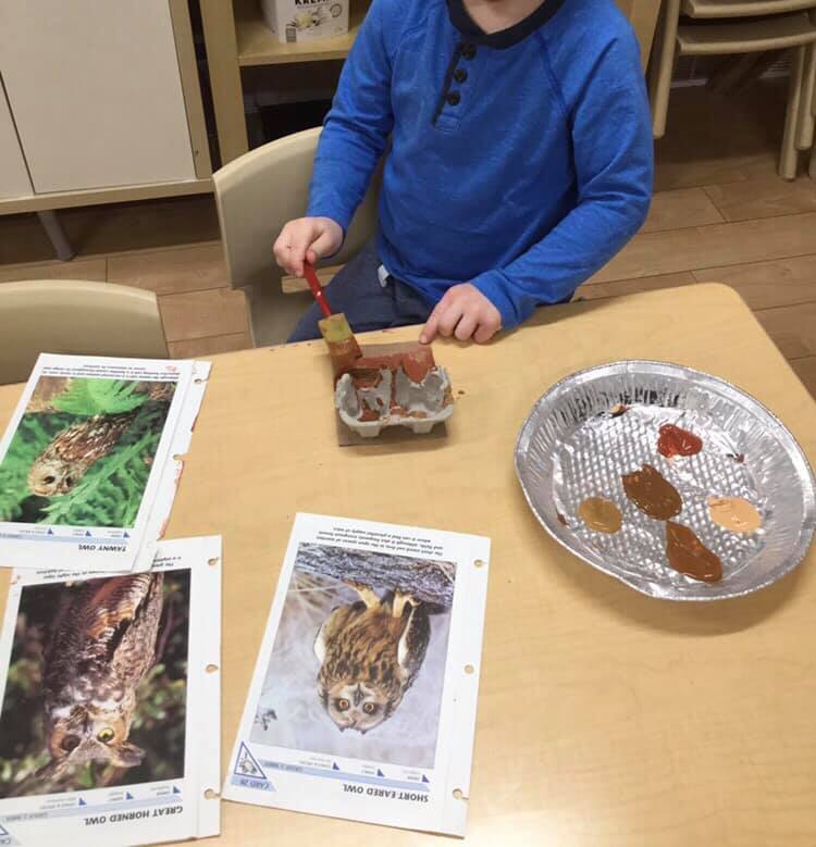 A boy in a blue shirt is sitting at a table painting a picture of a cat