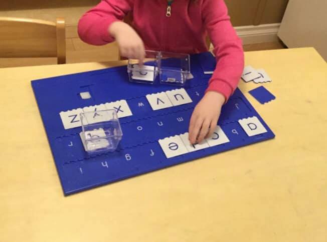 A little girl in a pink shirt is playing with letters on a blue board