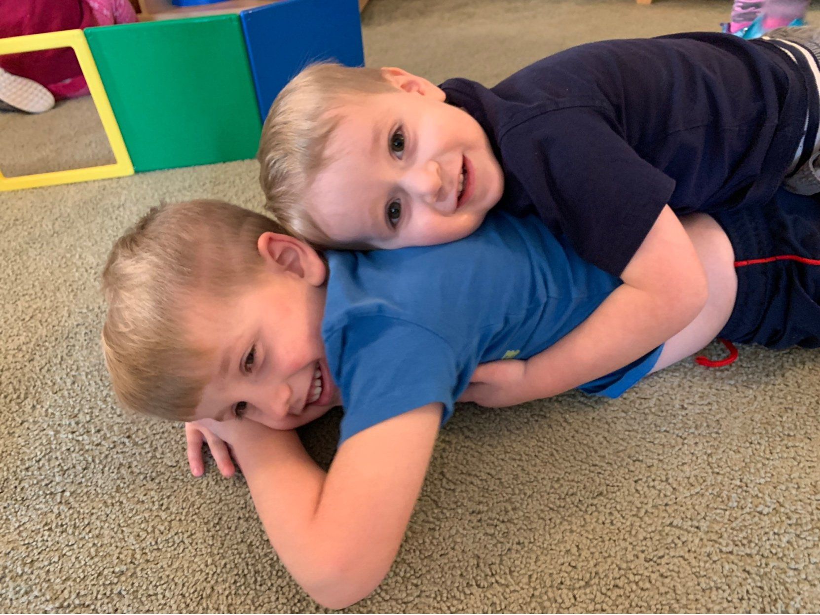 Two boys are laying on the floor hugging each other