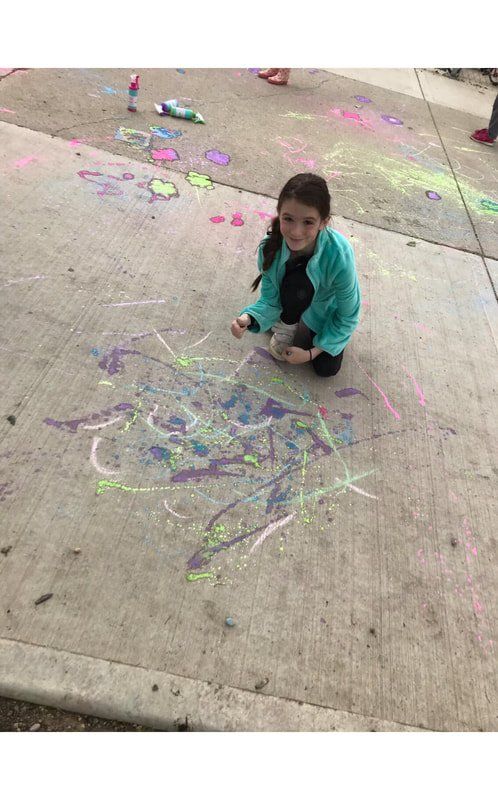 A little girl is kneeling on the sidewalk drawing with chalk.