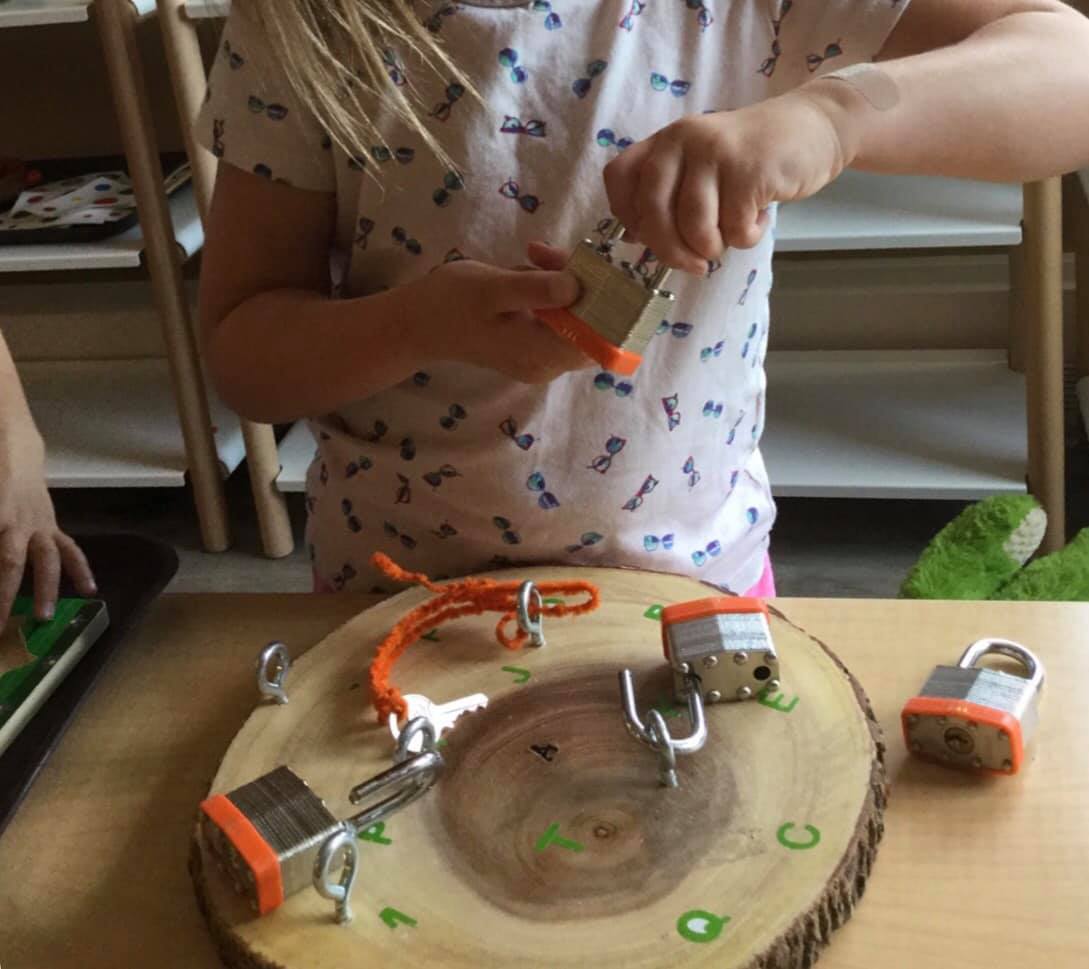 A little girl is playing with keys and locks on a wooden table