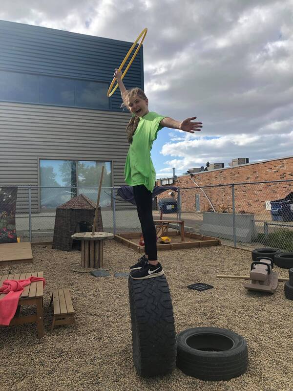A young girl is standing on top of a tire holding a hula hoop.