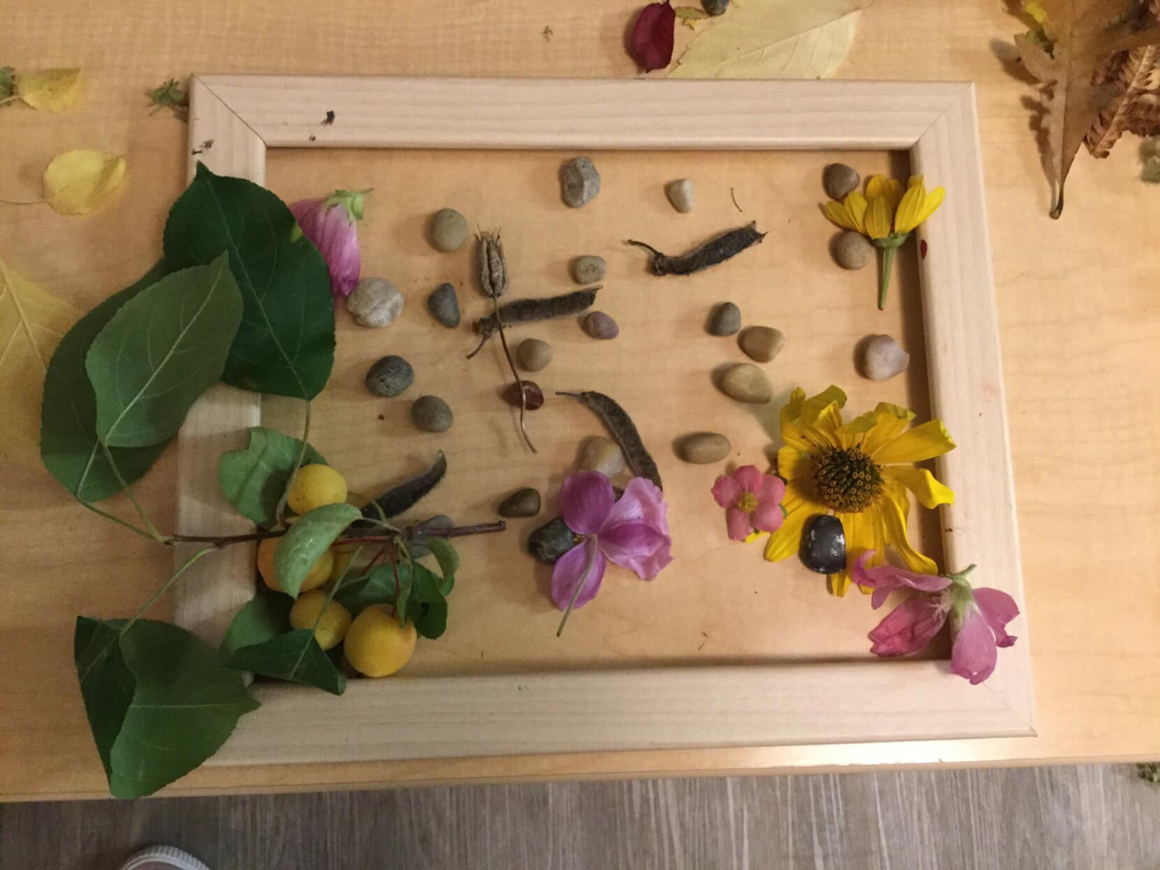 A picture frame filled with flowers and rocks on a wooden table.