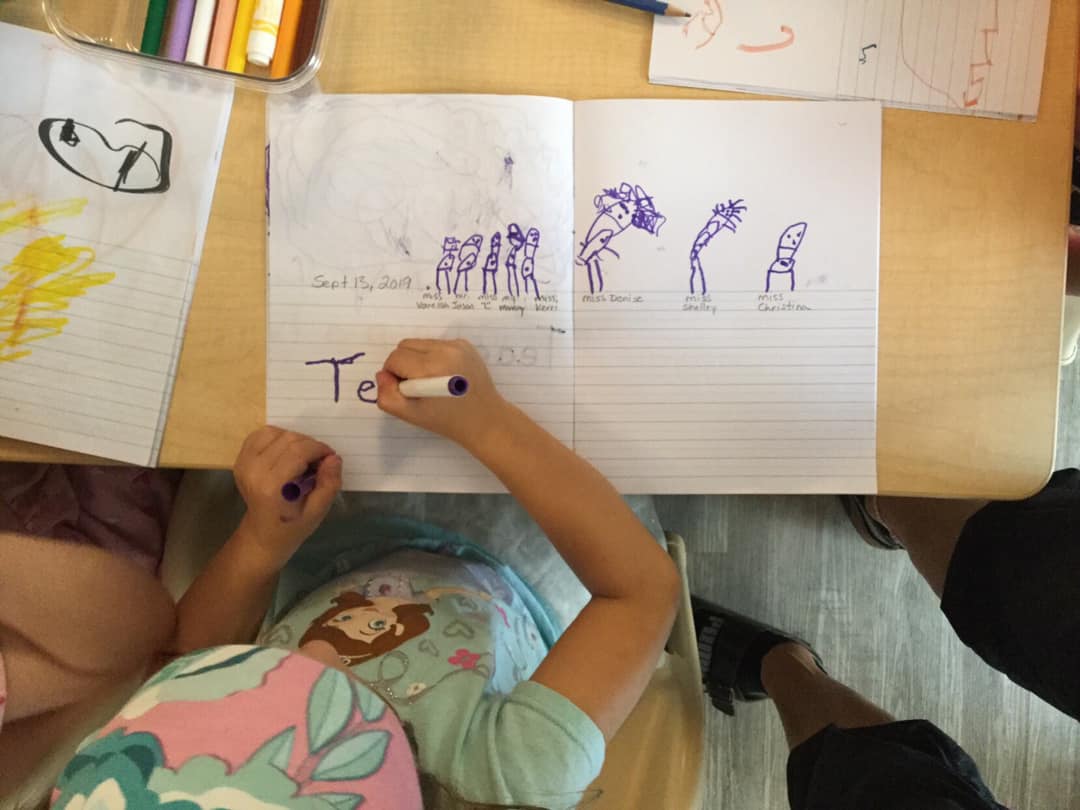 A child is writing the letter t on a piece of paper