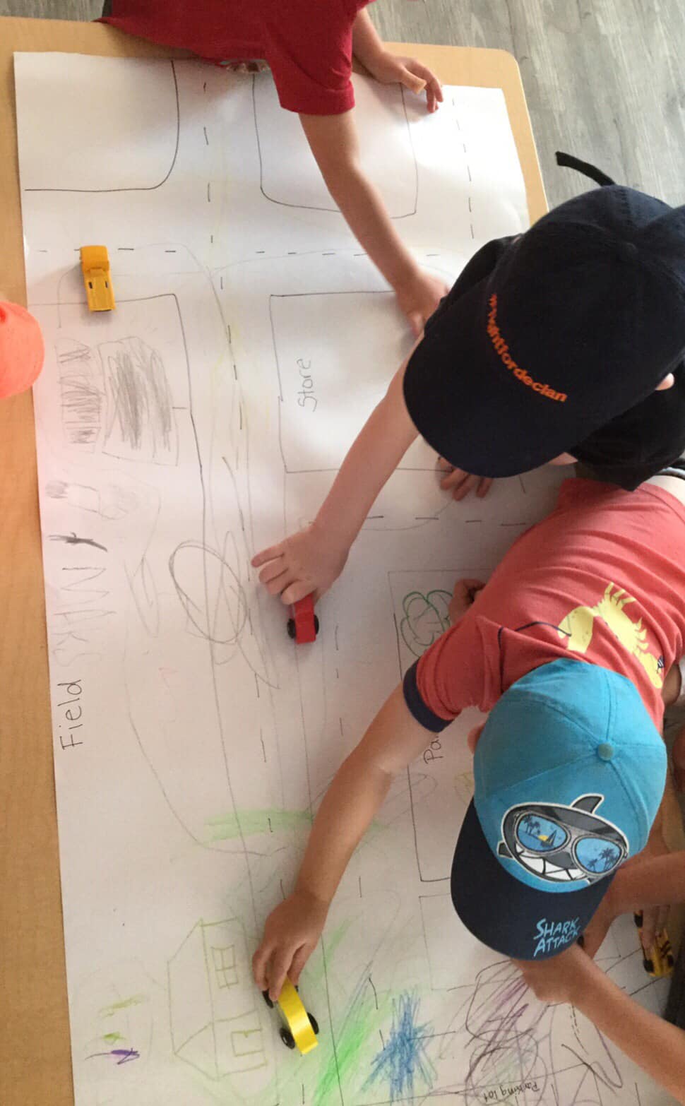 A group of children are playing with toy cars on a large piece of paper.