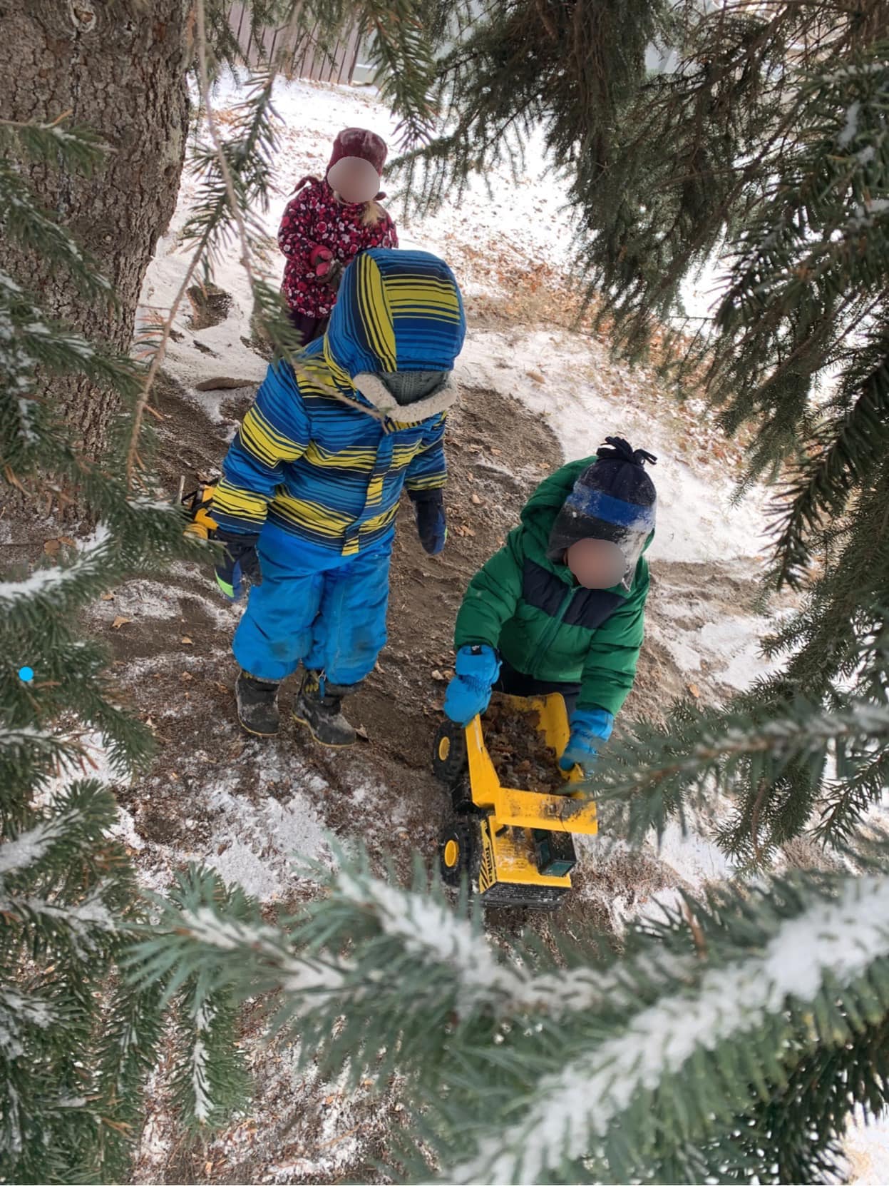 Three children are playing with a toy chainsaw in the snow.