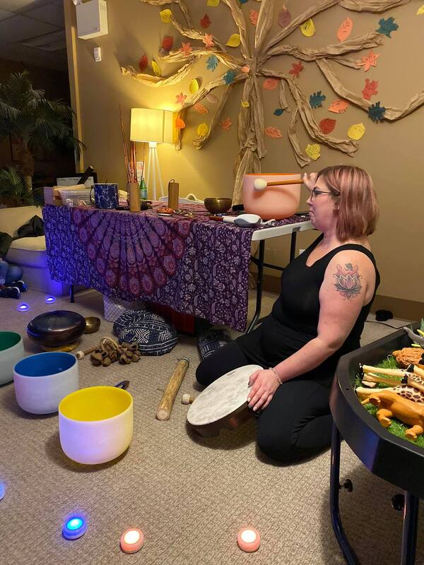 A woman is kneeling on the floor in a room surrounded by bowls and candles.