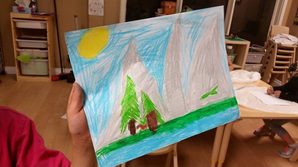 A person is holding a drawing of a mountain and trees.