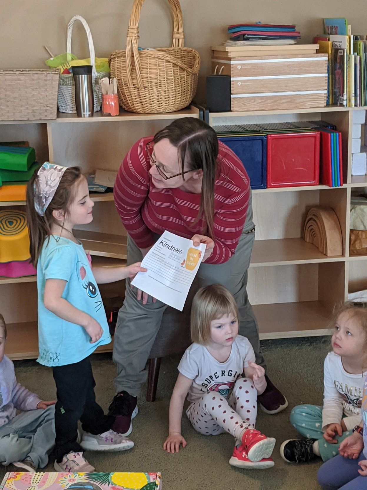 A woman is holding a piece of paper in front of a group of children.