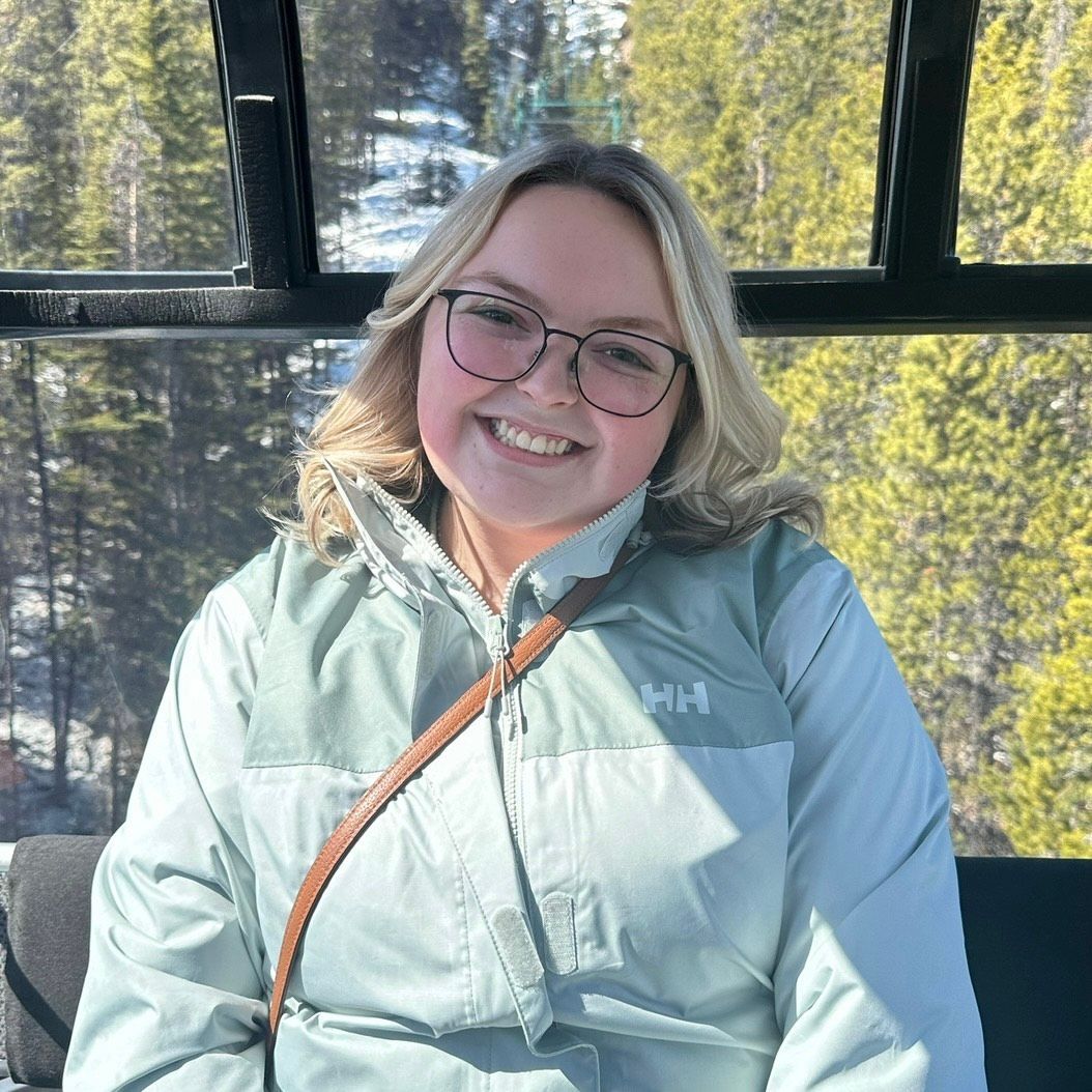 A woman is smiling while sitting in a car wearing a denim jacket.