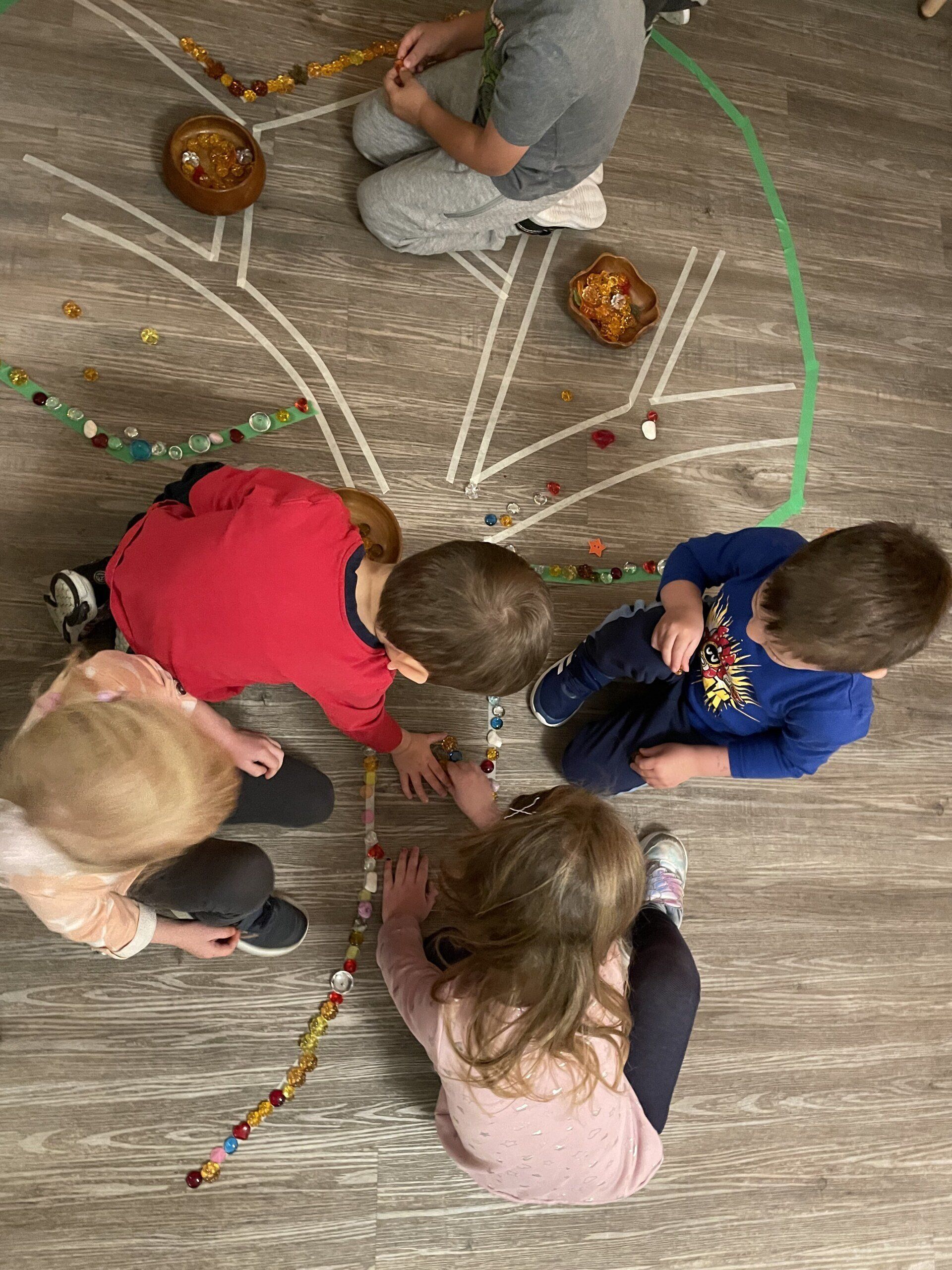A group of children are sitting on the floor playing with beads.