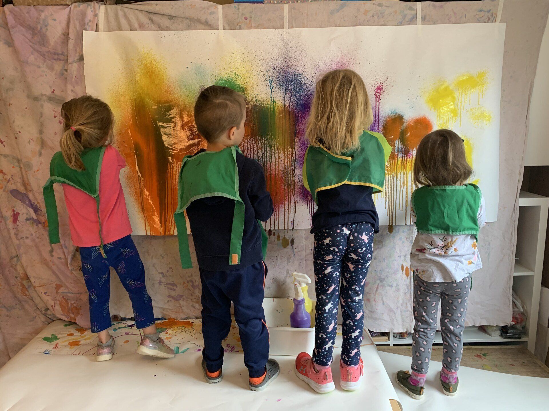 A group of children are standing in front of a large painting.