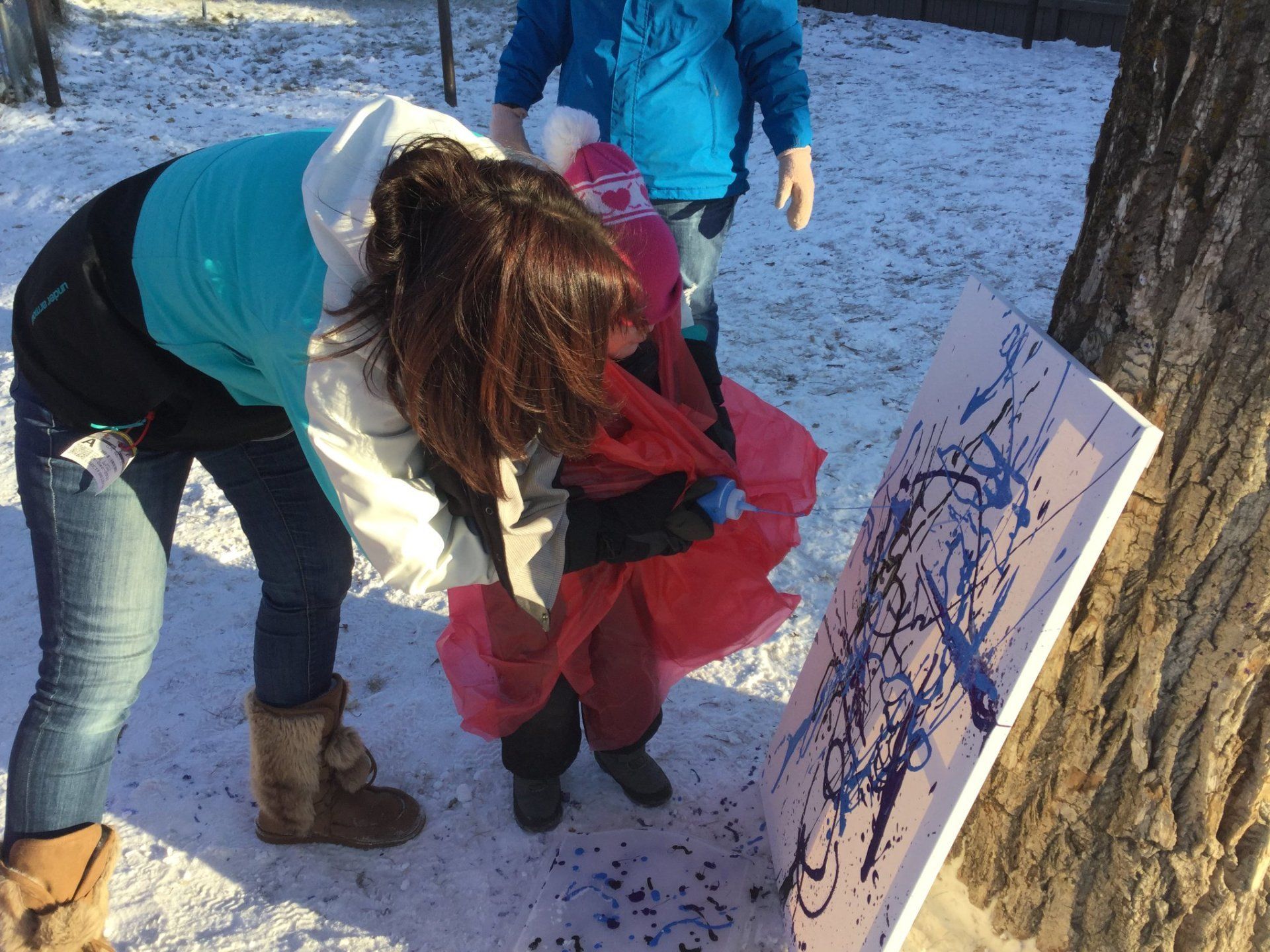 A woman and child are playing with a painting in the snow