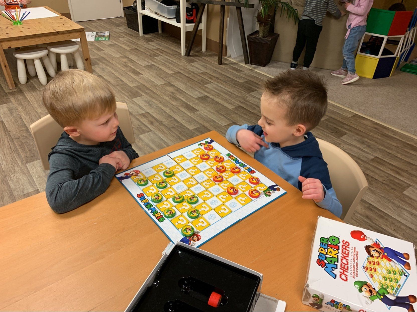 Two young boys are playing a game of checkers at a table.