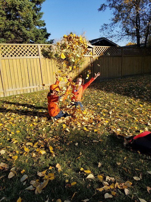 Two children are throwing leaves in the air in a backyard.