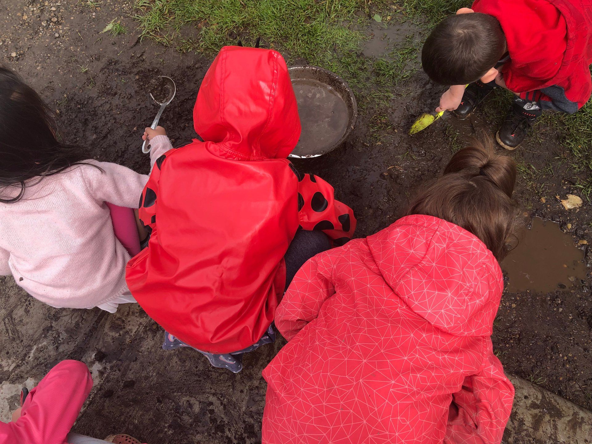 A group of children in red raincoats are playing in the mud.