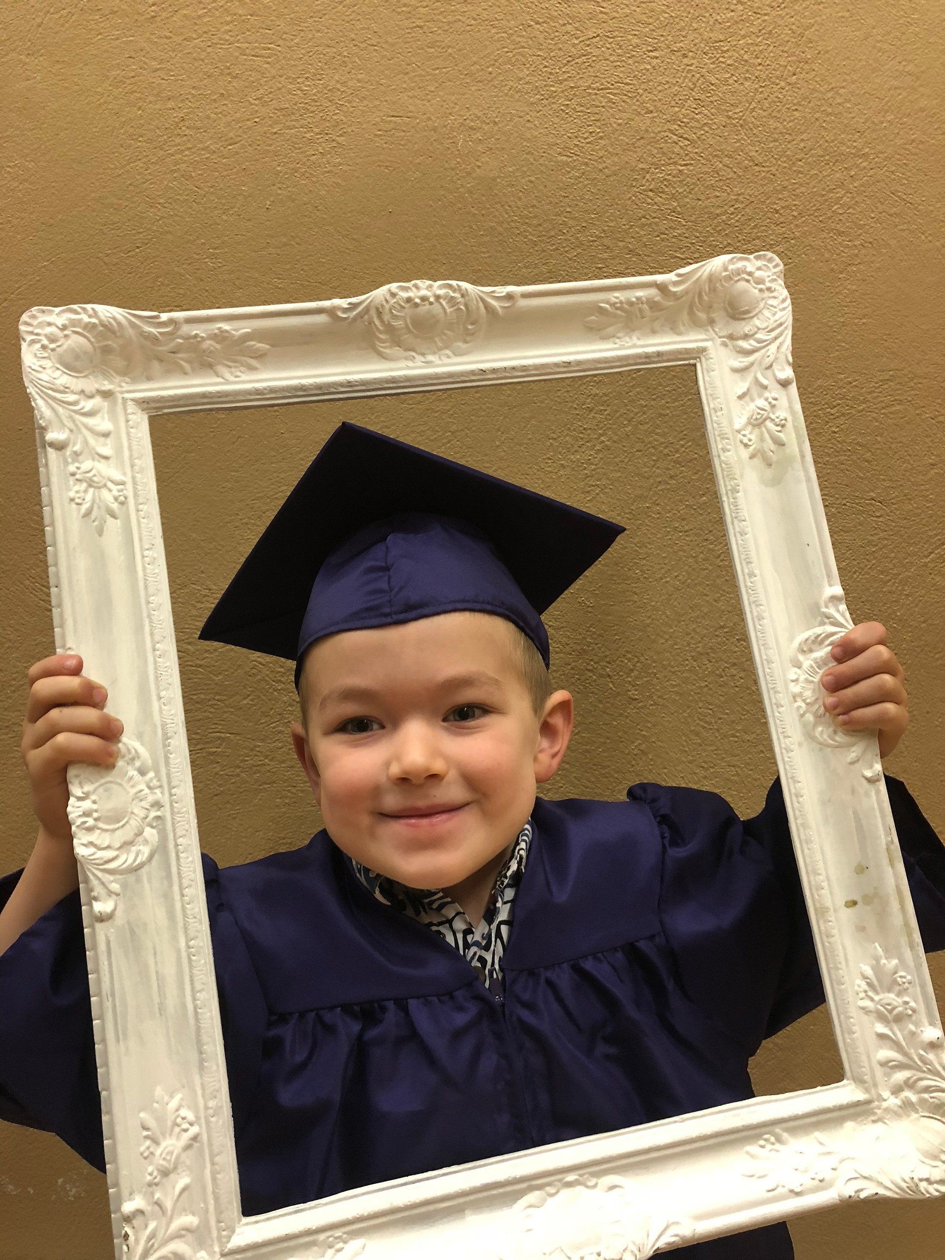 A young boy in a graduation cap and gown is holding a picture frame.