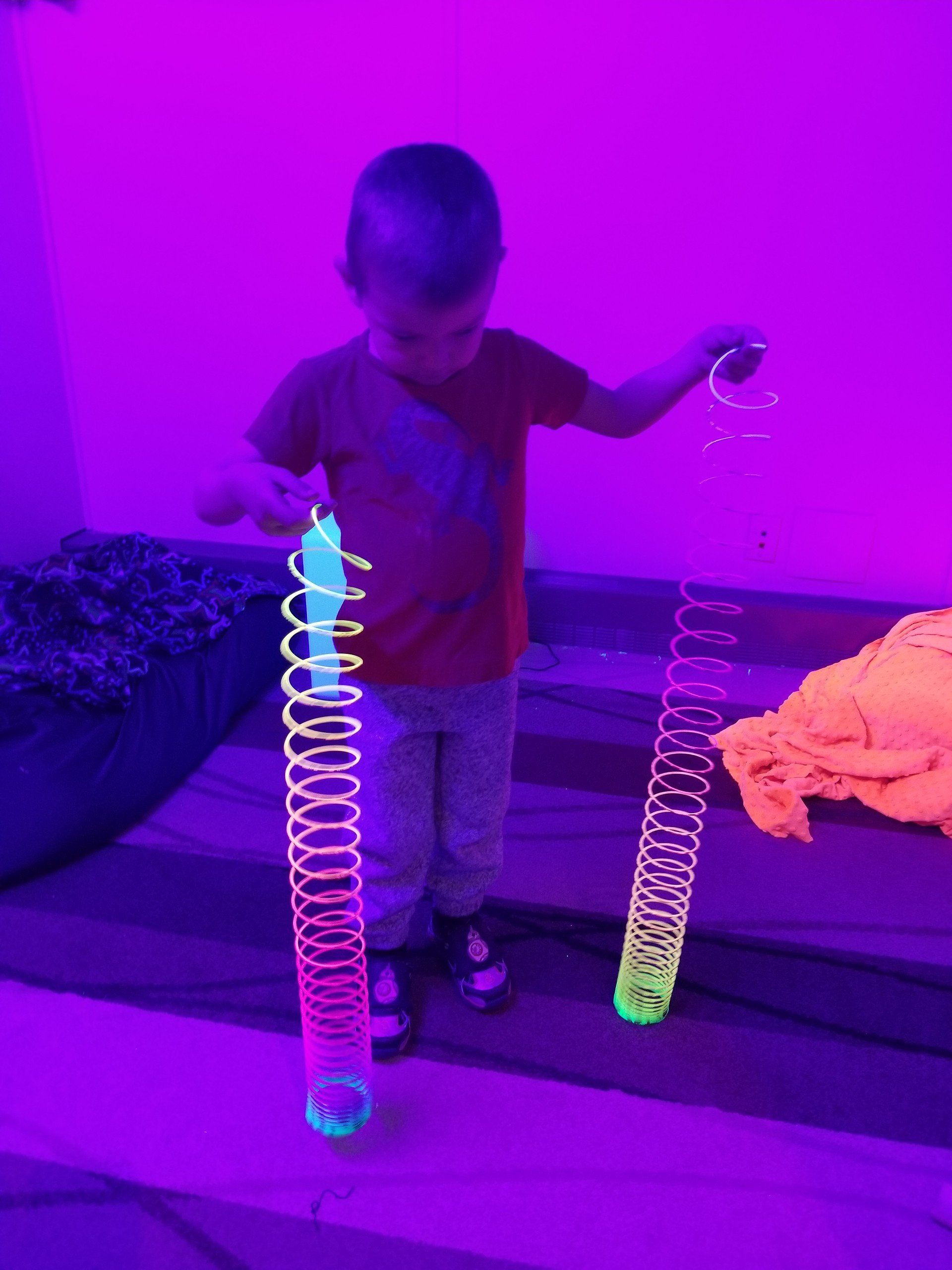 A young boy is playing with glow in the dark slinky springs.