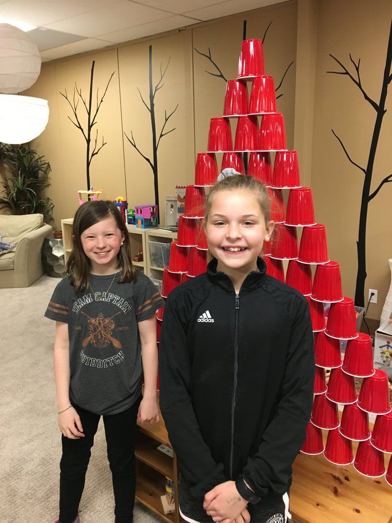 Two young girls are standing in front of a stack of red cups.