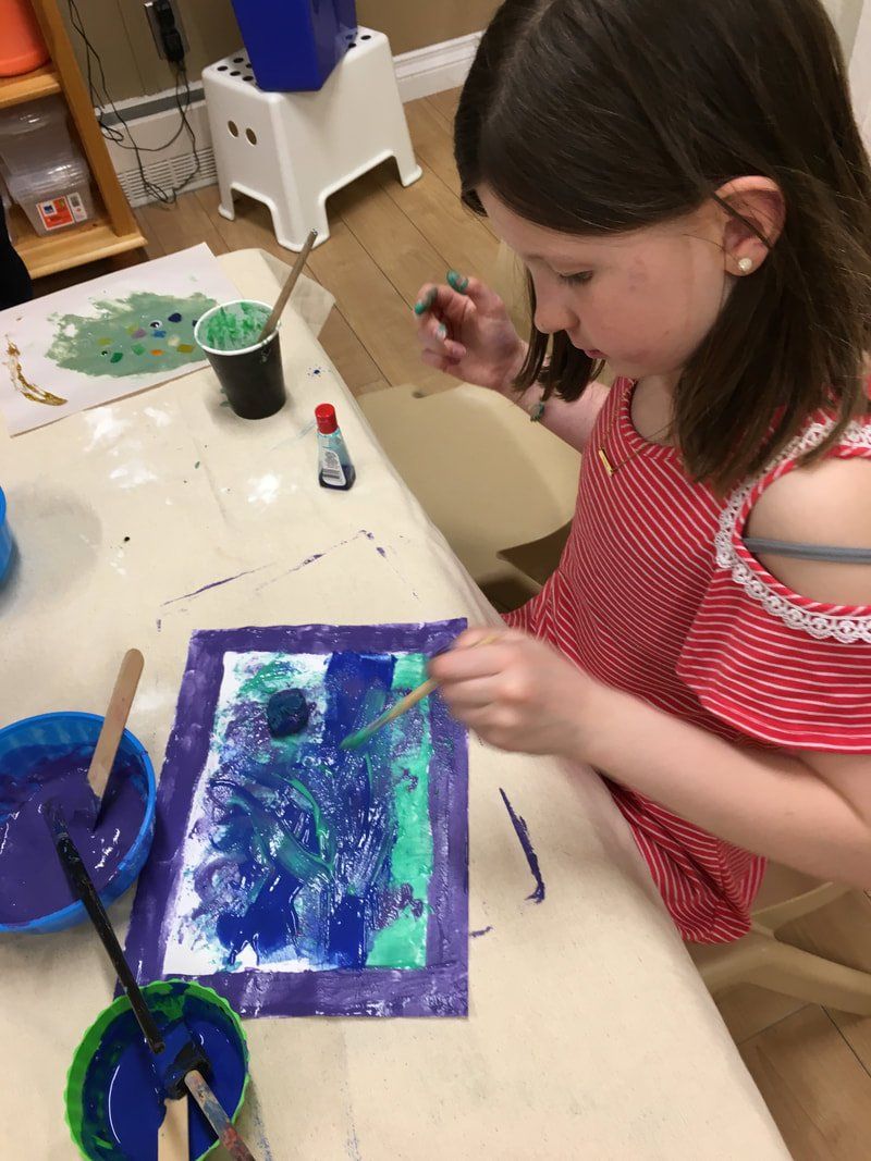 A little girl is sitting at a table painting a picture