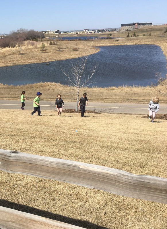 A group of children are running in a field near a lake.