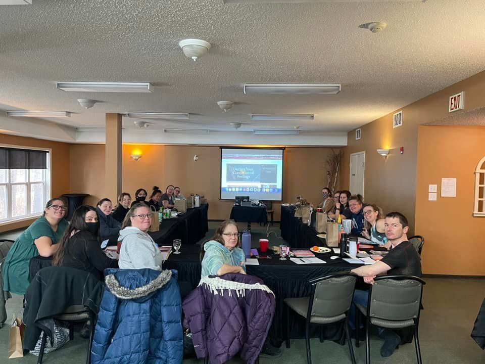 A group of people are sitting at tables in a room with a projector screen.