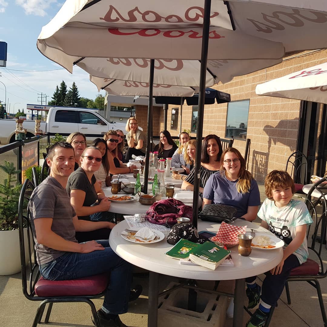 A group of people are sitting at a table under an umbrella that says coors light