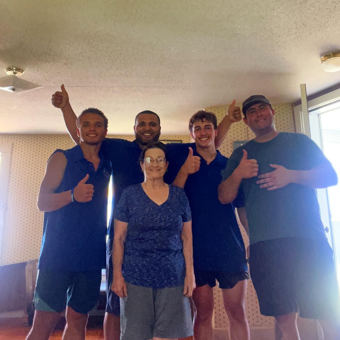 Group of five people indoors, smiling and giving thumbs up.