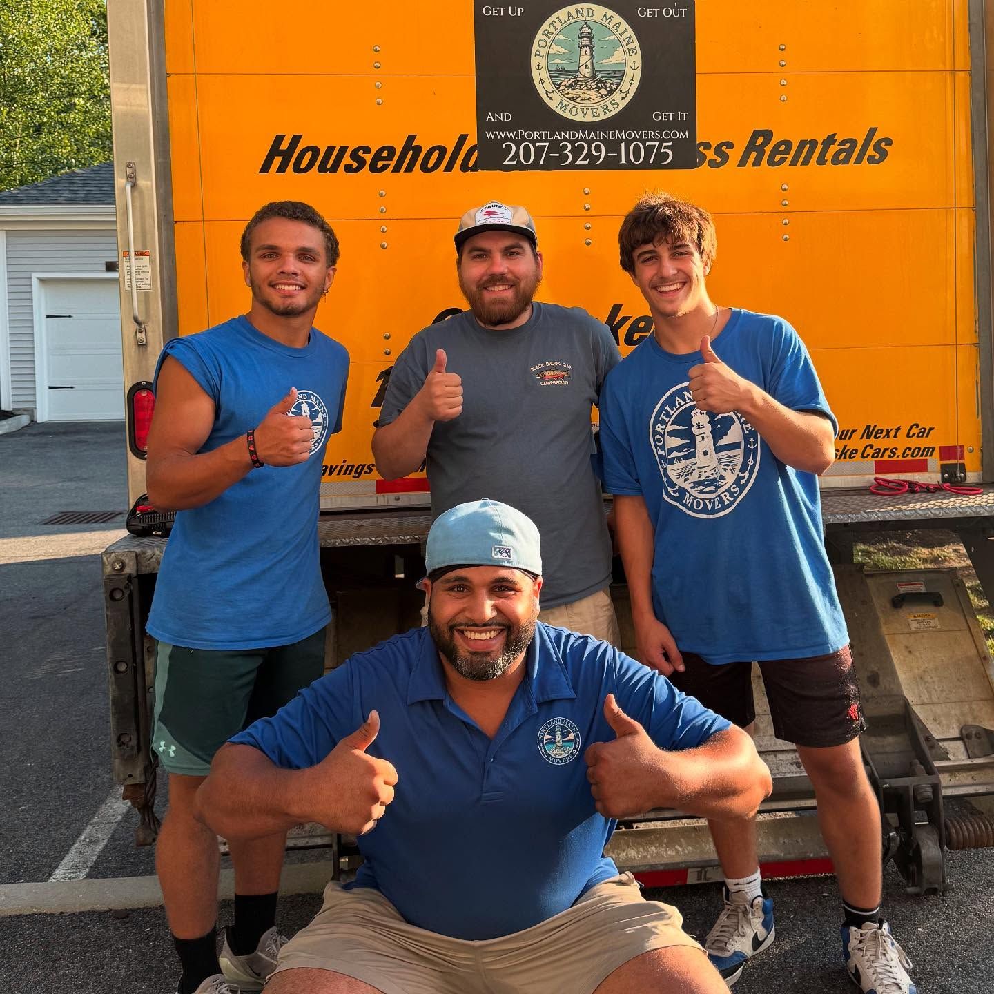 Four men standing in front of a yellow moving truck giving thumbs up.