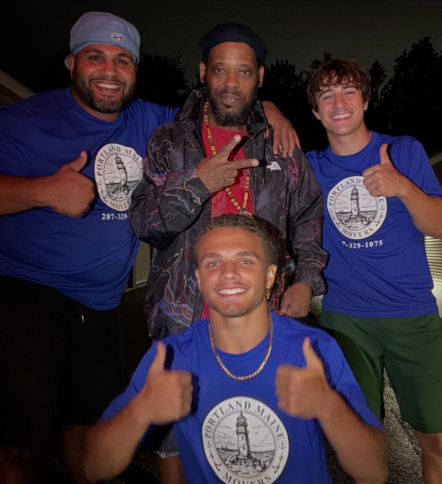Four people in blue shirts with a lighthouse logo give thumbs up. One person wears a jacket, and another smiles.