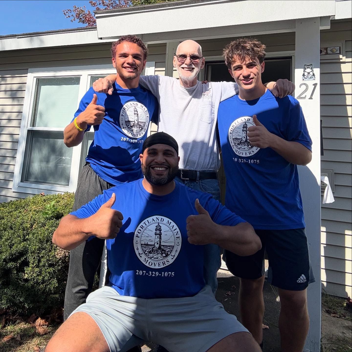 Four people in blue shirts with a lighthouse logo pose outside a house, giving thumbs up.