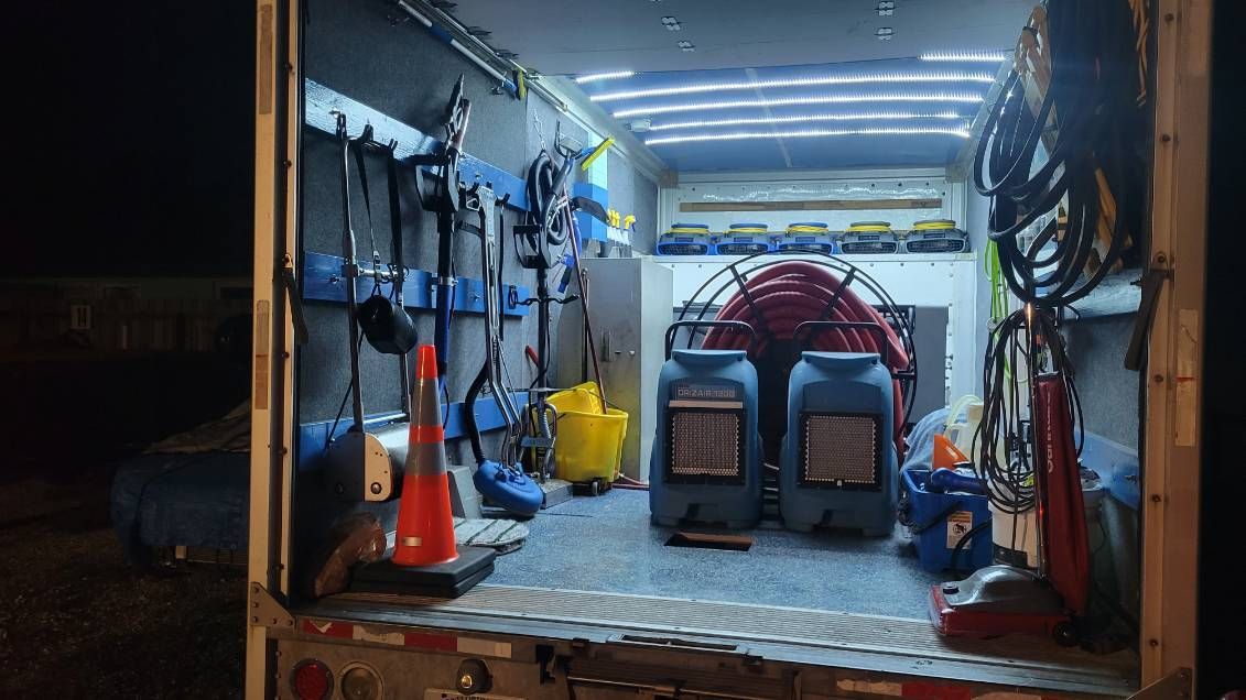 Inside a flood cleanup truck; equipment is stored on walls. Includes blue, yellow, and red tools, and large blue containers.