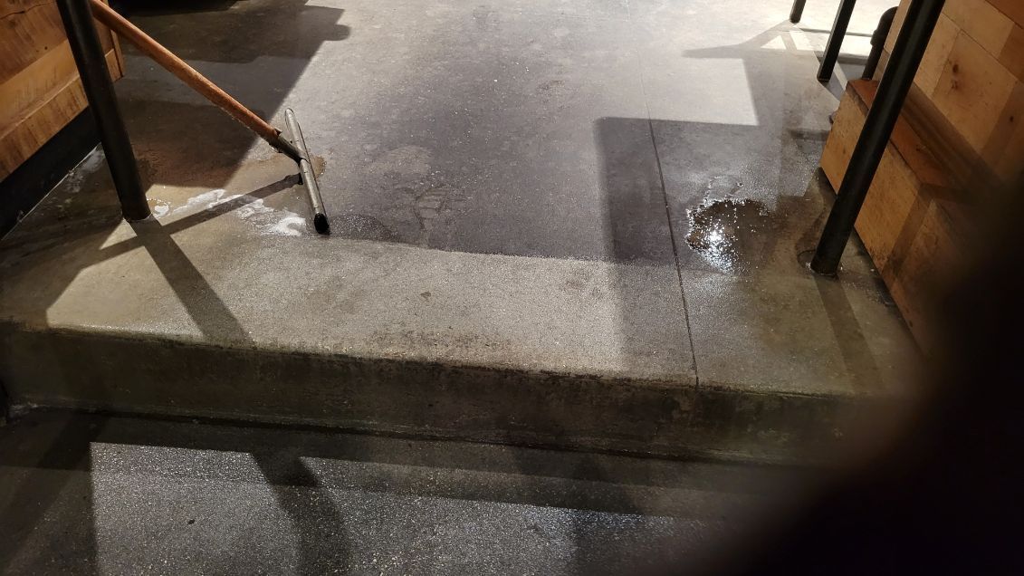 Concrete steps leading down, wet surface with a broom in use; interior setting with wooden paneling.