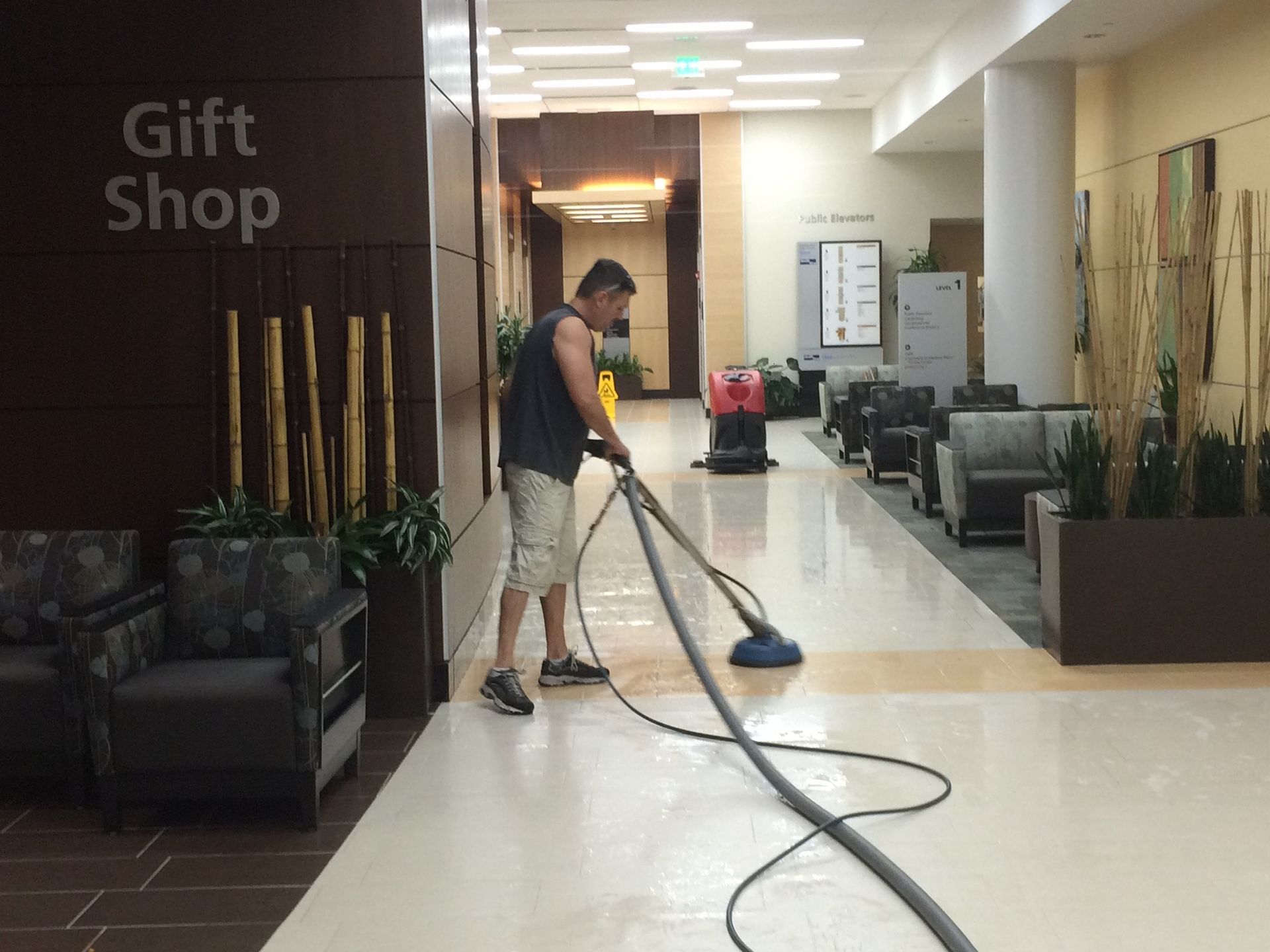 A person cleans a shiny, wet floor in a hallway with a large floor cleaner. 