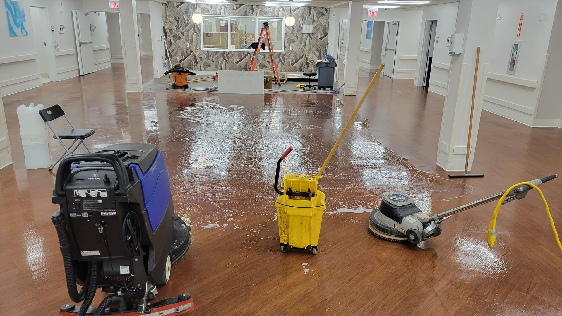 Wooden floor being cleaned with a machine, mop, and bucket.