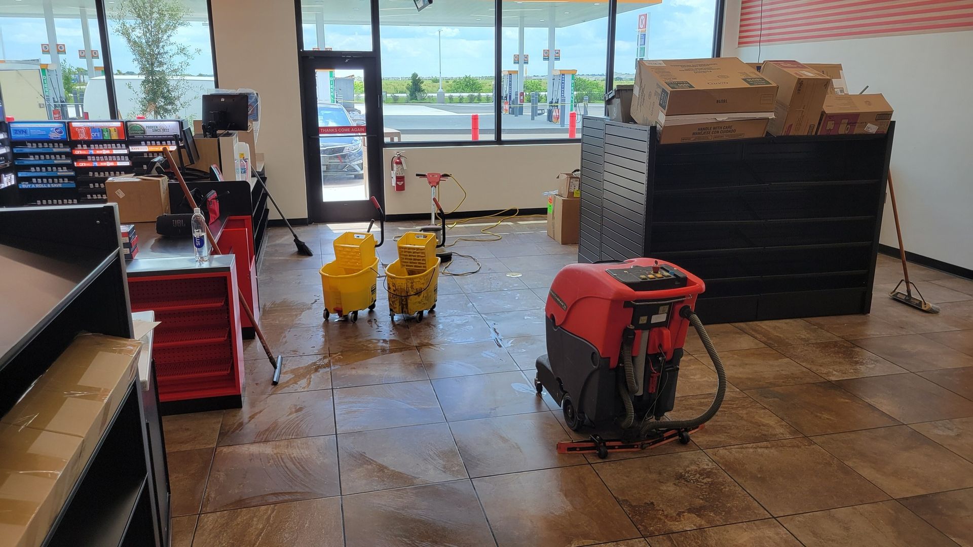 Inside a convenience store, cleaning in progress: a floor scrubber, mop buckets, and boxes on shelves.