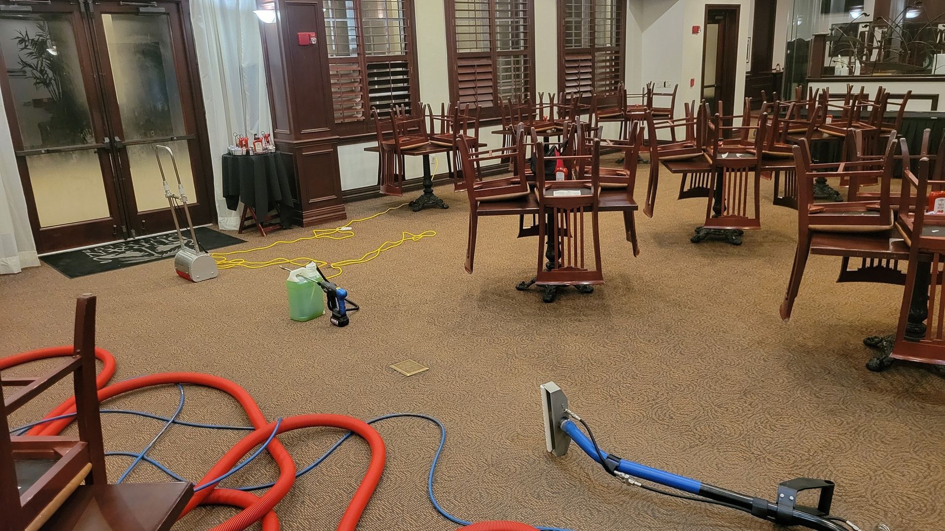 Carpet cleaning equipment in a dining room with chairs stacked on tables.