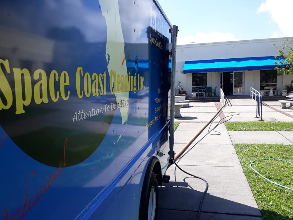 Blue Space Coast Plumbing truck parked on a sidewalk next to a building with a blue awning.