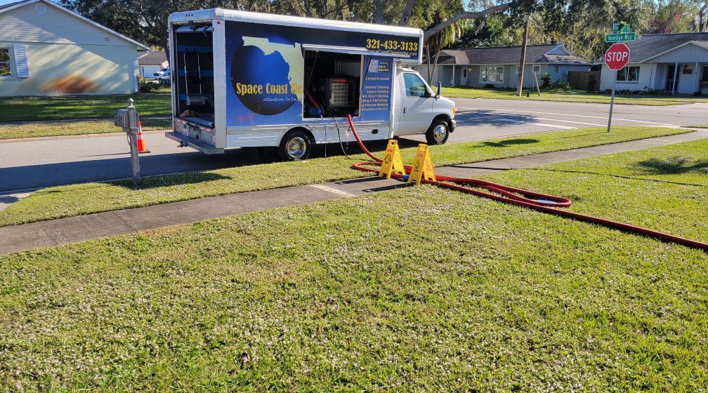 A white work van with hoses extending to a lawn. The van has a Florida graphic.