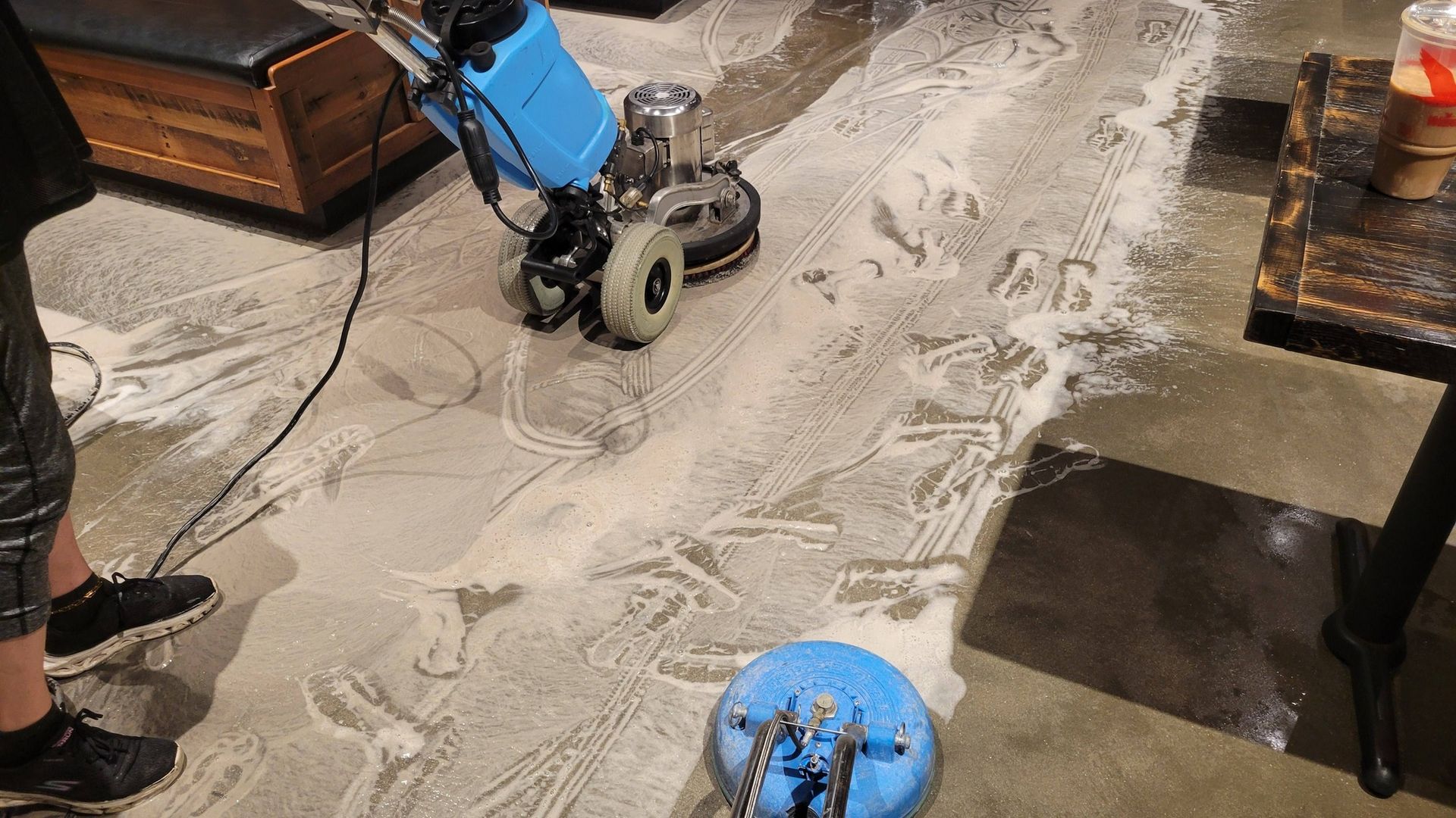 A floor cleaning machine scrubbing a concrete floor, creating foam.