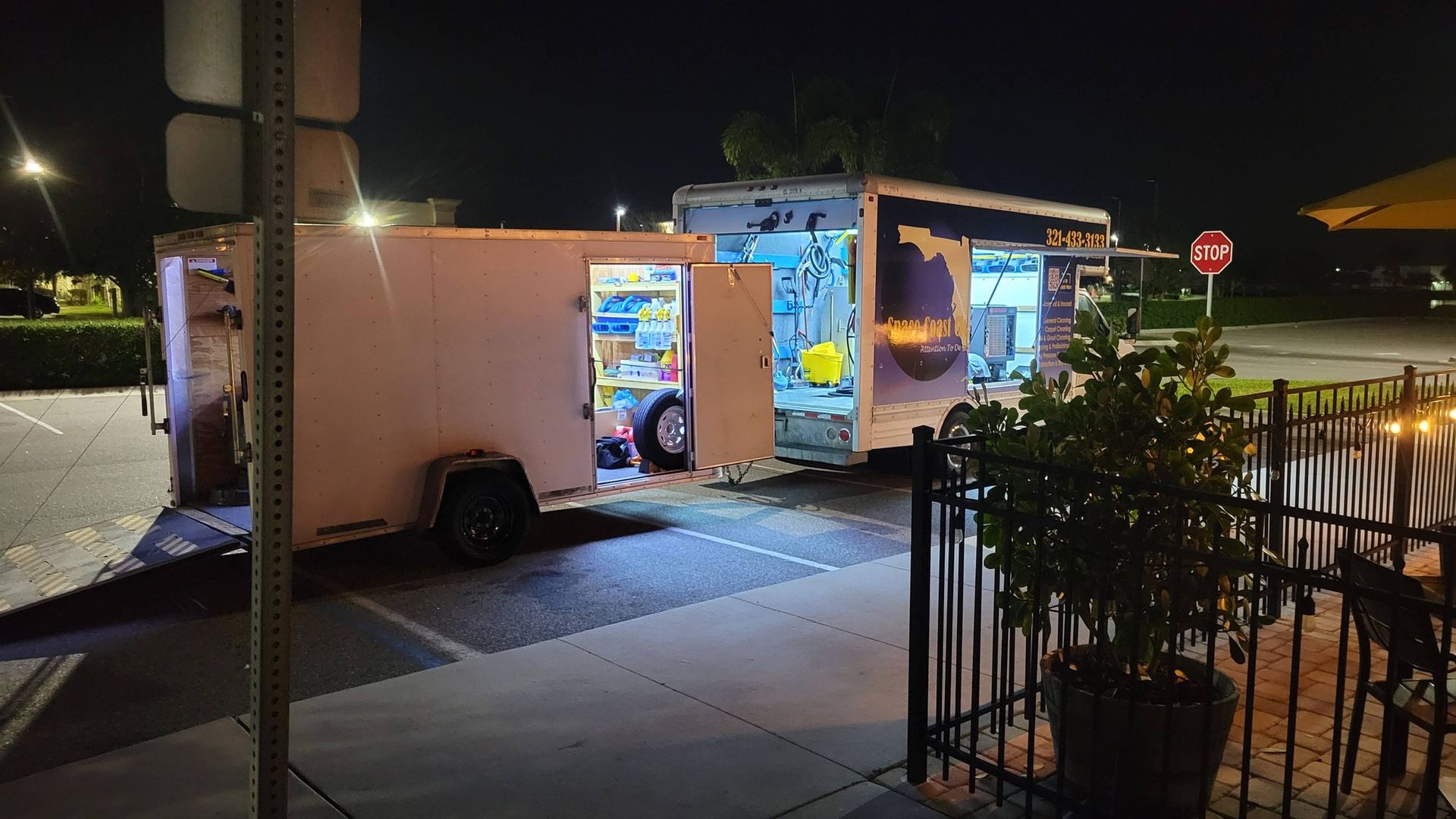 Food trailer at night, with open serving windows, illuminated interior, and a plant in a pot.