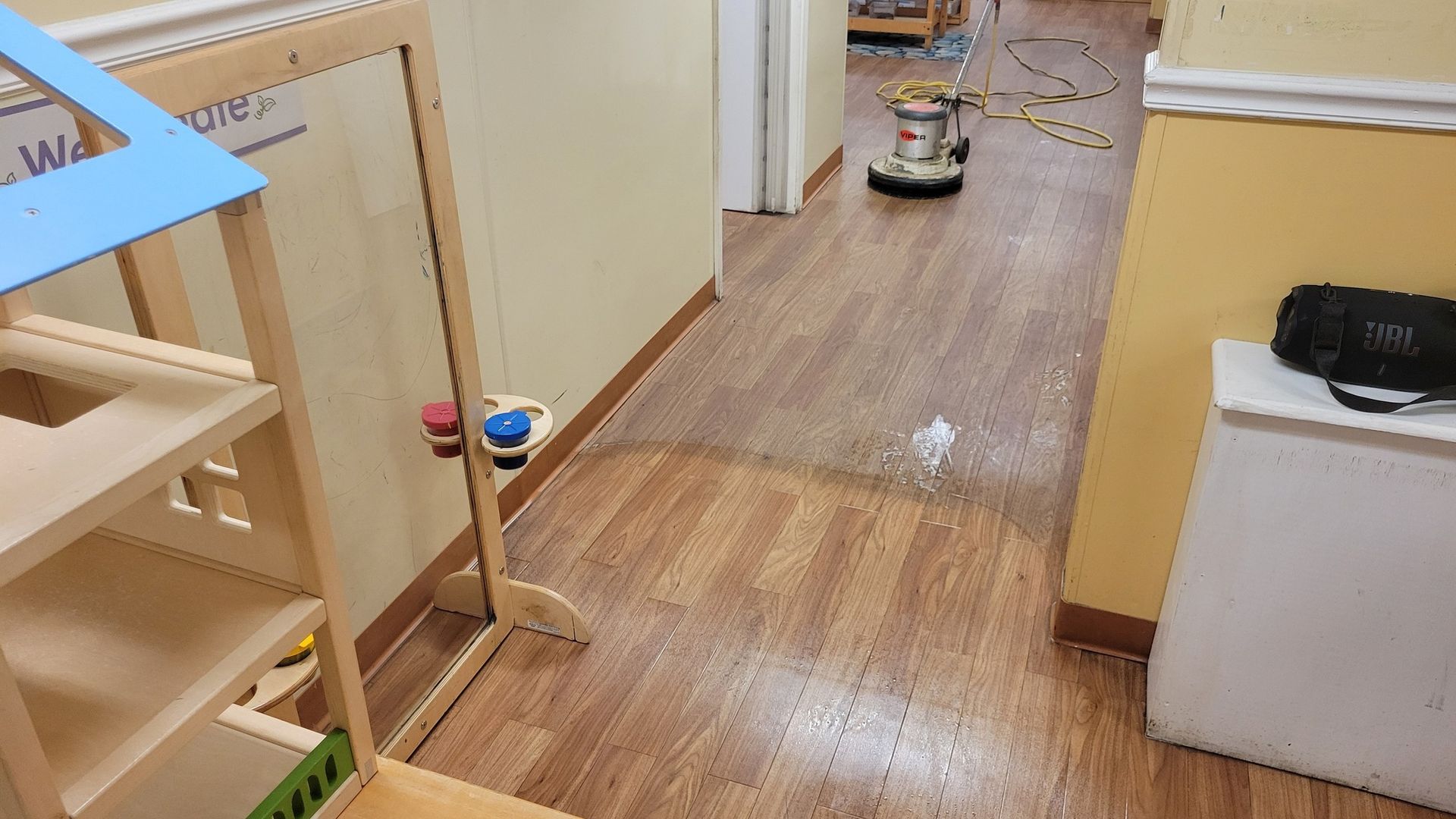 Wooden floor being cleaned in a hallway with a floor polisher. A toy house is on the left.