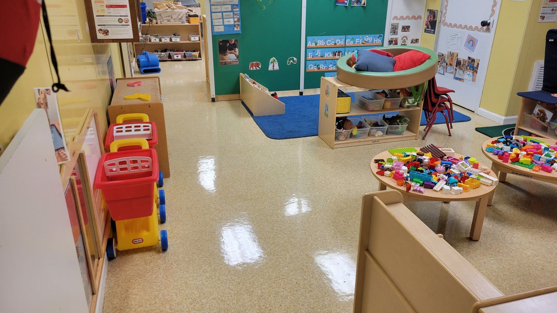 Childcare classroom interior with toys, tables, and play areas.
