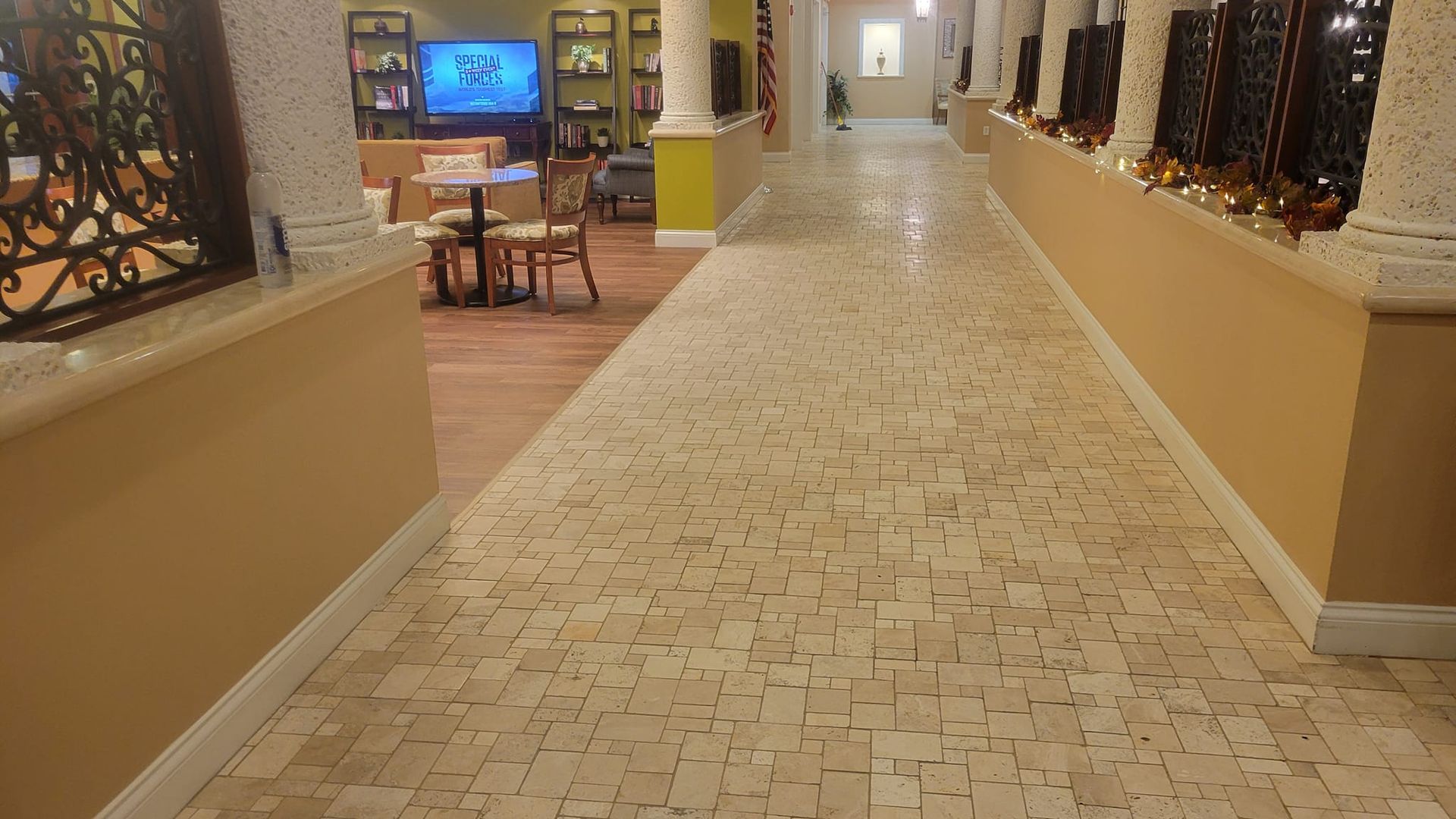 Hallway with mosaic tile floor, beige walls, ornate railing, and seating area in the background.